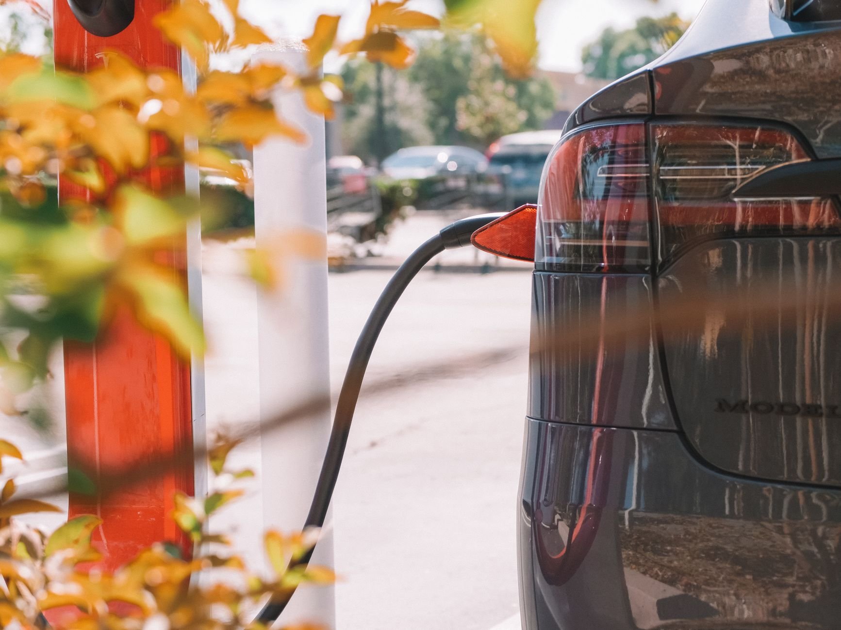 Close-up of an electric car charging at a station, with other vehicles in the background.